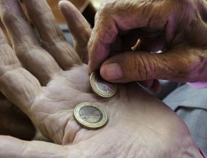Nahaufnahme Händer alter Frau. Rechte Hand legt zwei 1€-Stücke auf linke Hand.